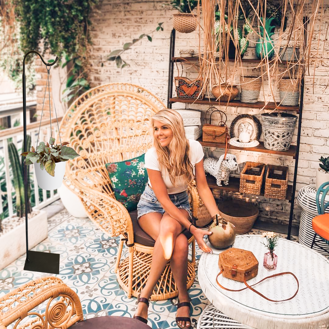 Woman sitting on a wicker chair in a cozy, decorated room with plants and shelves.
