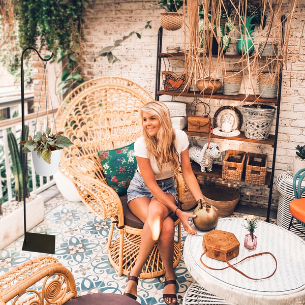Woman sitting on a wicker chair in a cozy, decorated room with plants and shelves.