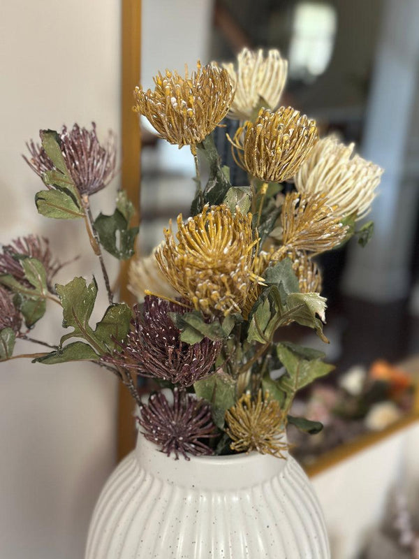 Decorative bouquet with gold and purple flowers in a white vase against a blurred indoor background