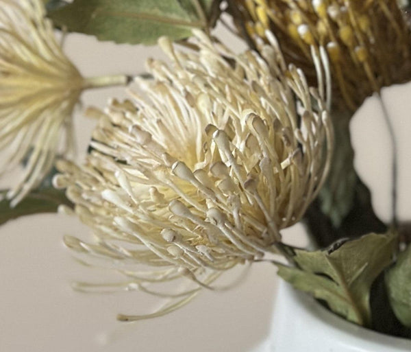 Close-up of a gold artificial flower with green leaves on a white background