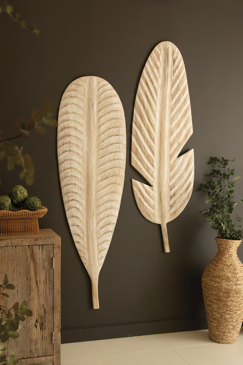 Decorative leaf-shaped wall art on a dark wall with a wooden cabinet and vase.