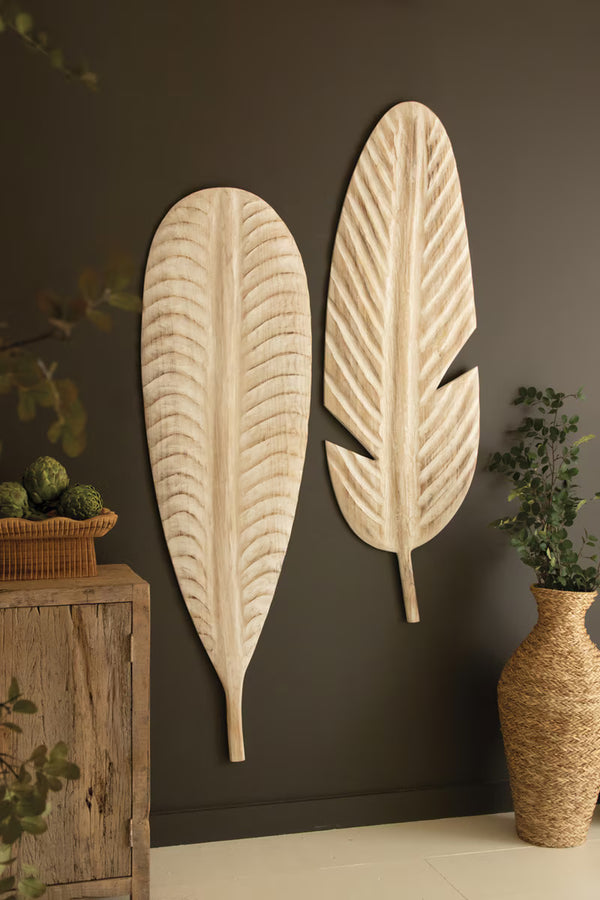 Decorative leaf-shaped wall art on a dark wall with a wooden cabinet and vase.