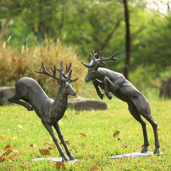 Bronze deer statues on a grassy area with trees in the background