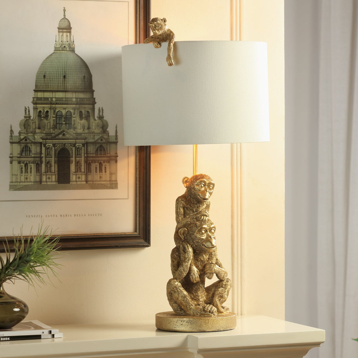 Decorative lamp with monkey design on a table next to a framed picture of a building.