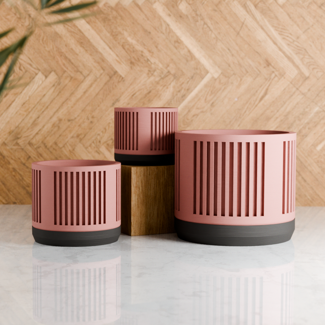 Three pink planters with black bases on a light surface against a wooden background