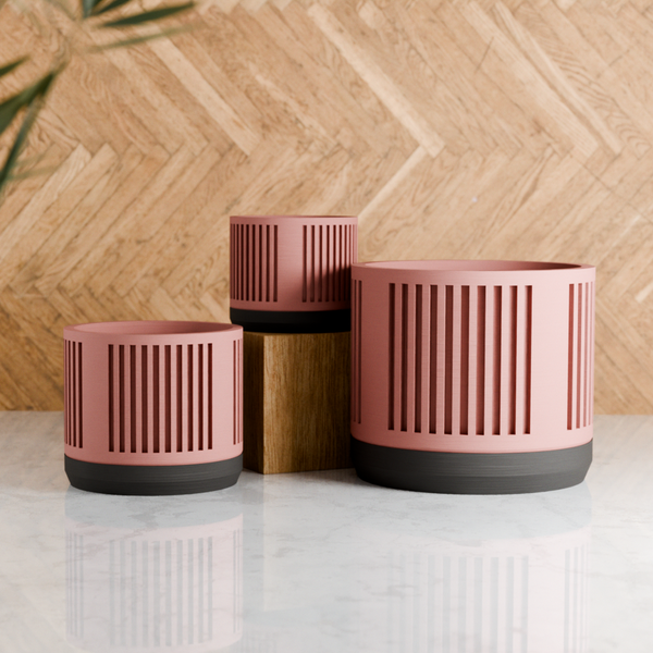Three pink planters with black bases on a light surface against a wooden background