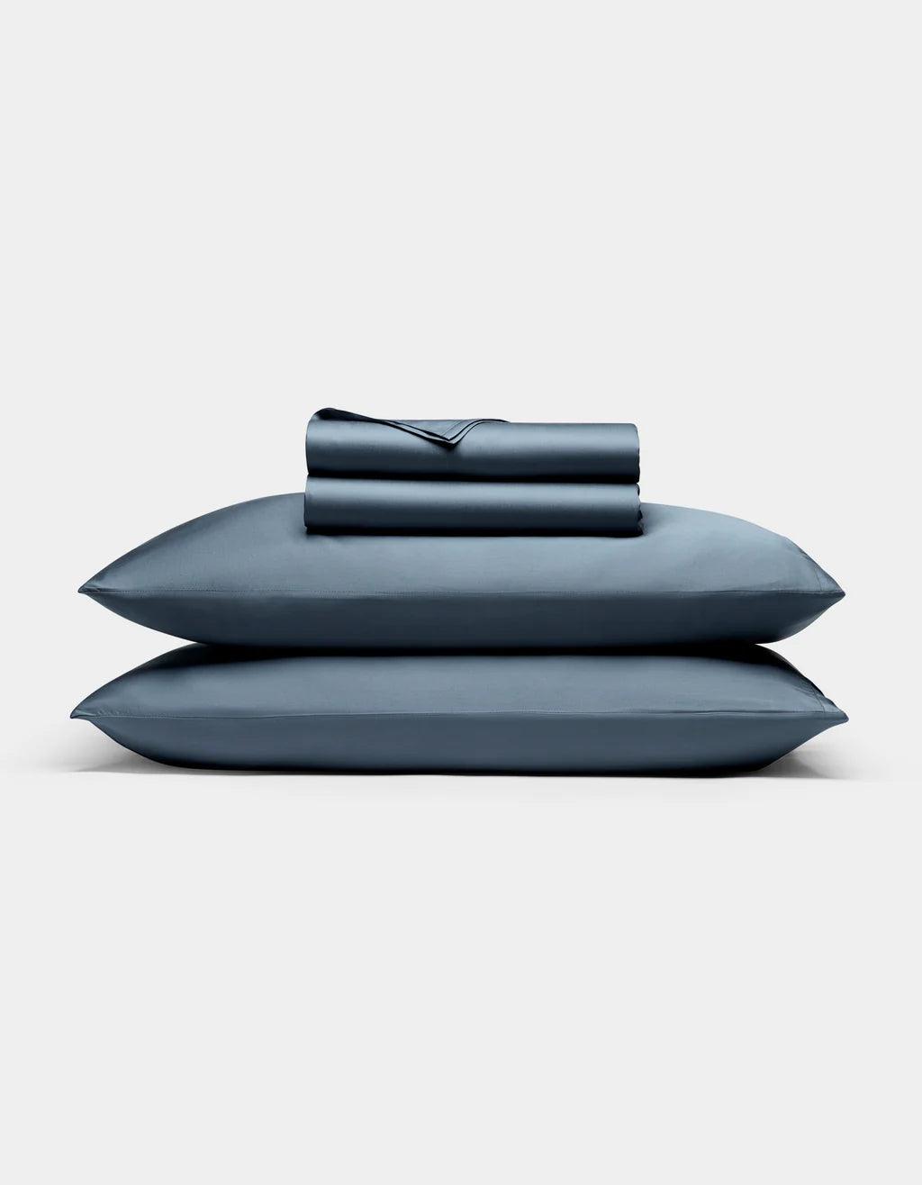 Pacific Blue - Set of blue bedding including a pillow and two folded sheets on a light gray background