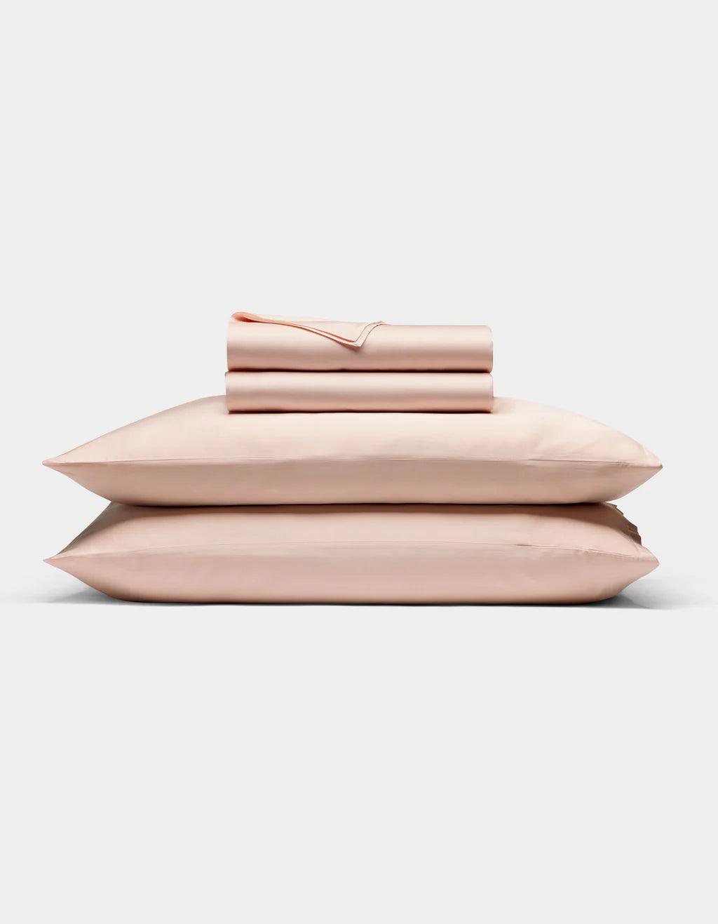 Peony - Set of pink bedding including a duvet, two pillows, and a folded blanket on a light gray background.