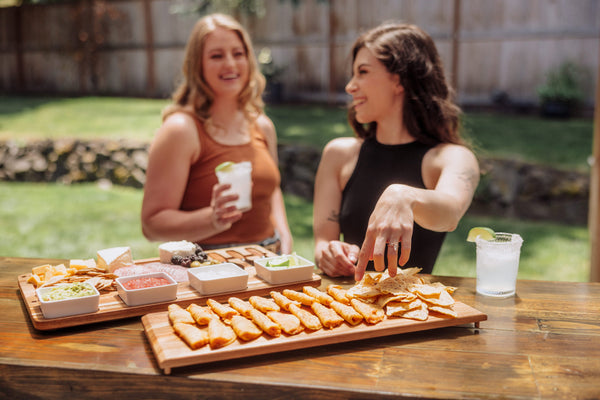 Two women enjoying snacks and drinks at a outdoor gathering.