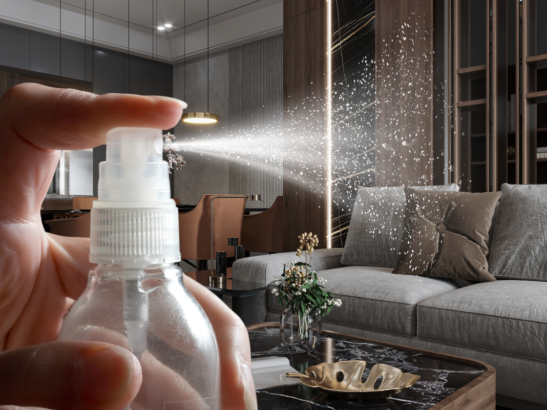 Hand holding a spray bottle with mist in a modern living room.