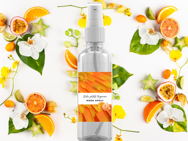 Room spray bottle with orange and white design surrounded by fruits and flowers on a white background