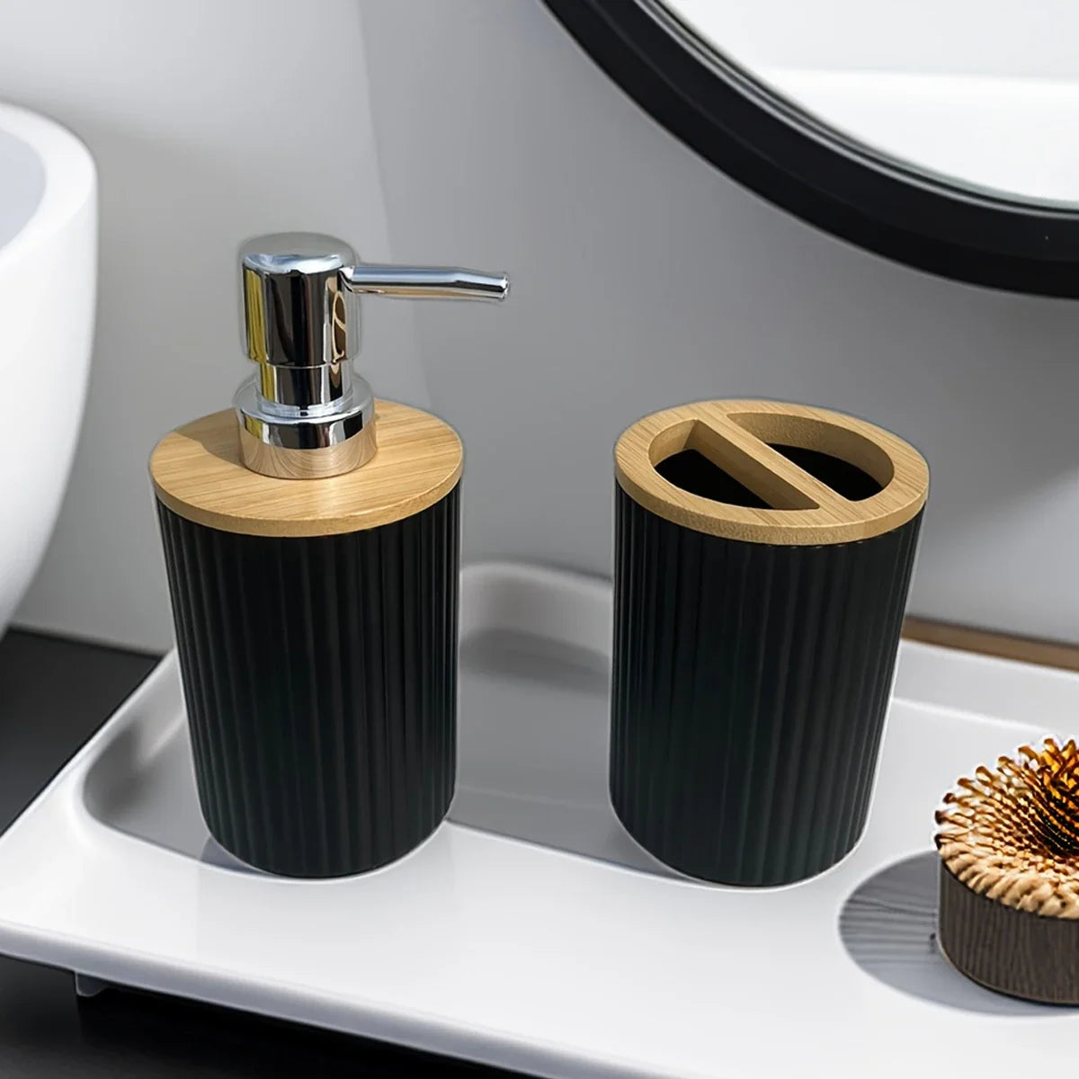 Close-up of Buddify black bathroom accessories set with bamboo top soap dispenser and toothbrush holder on white tray near mirror.