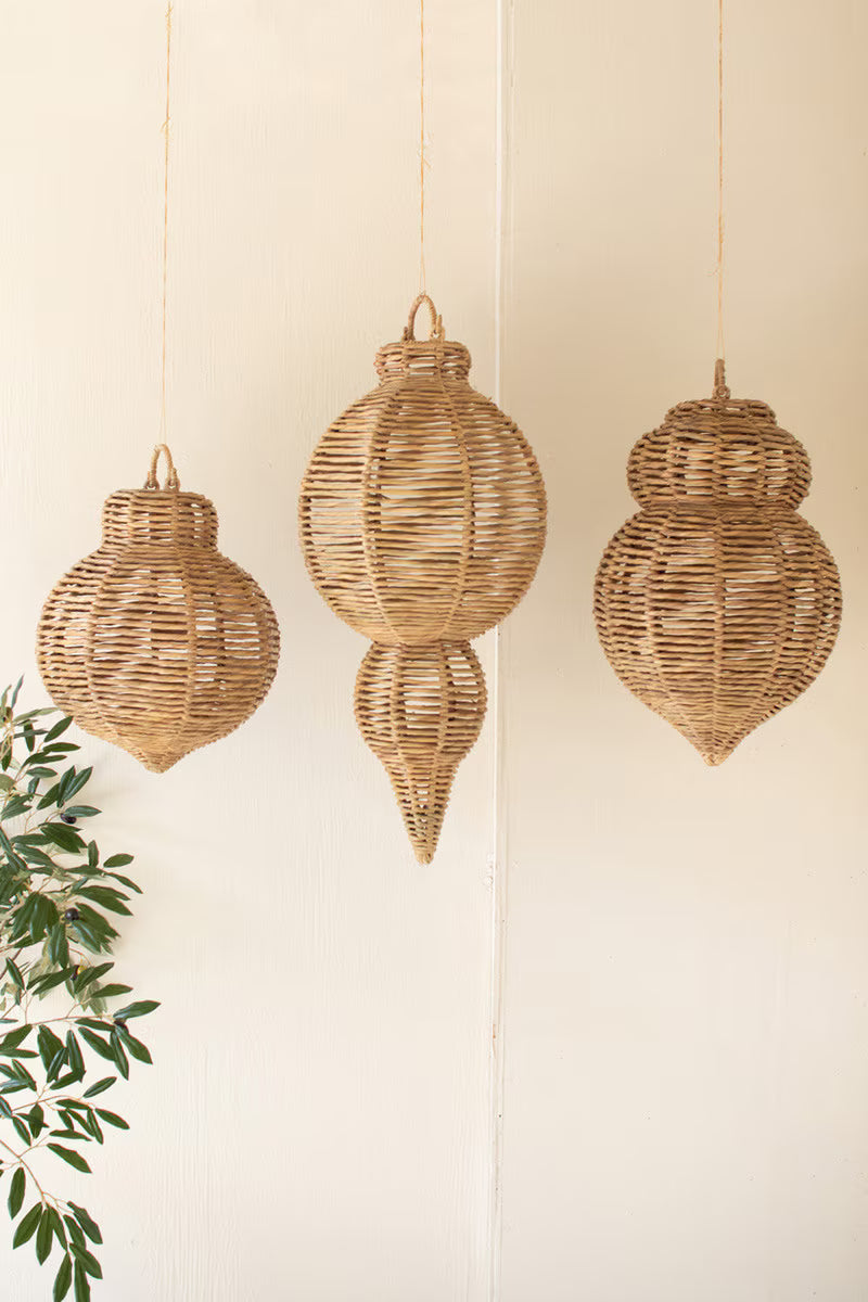 Three wicker hanging lanterns on a white wall with a green plant to the left.