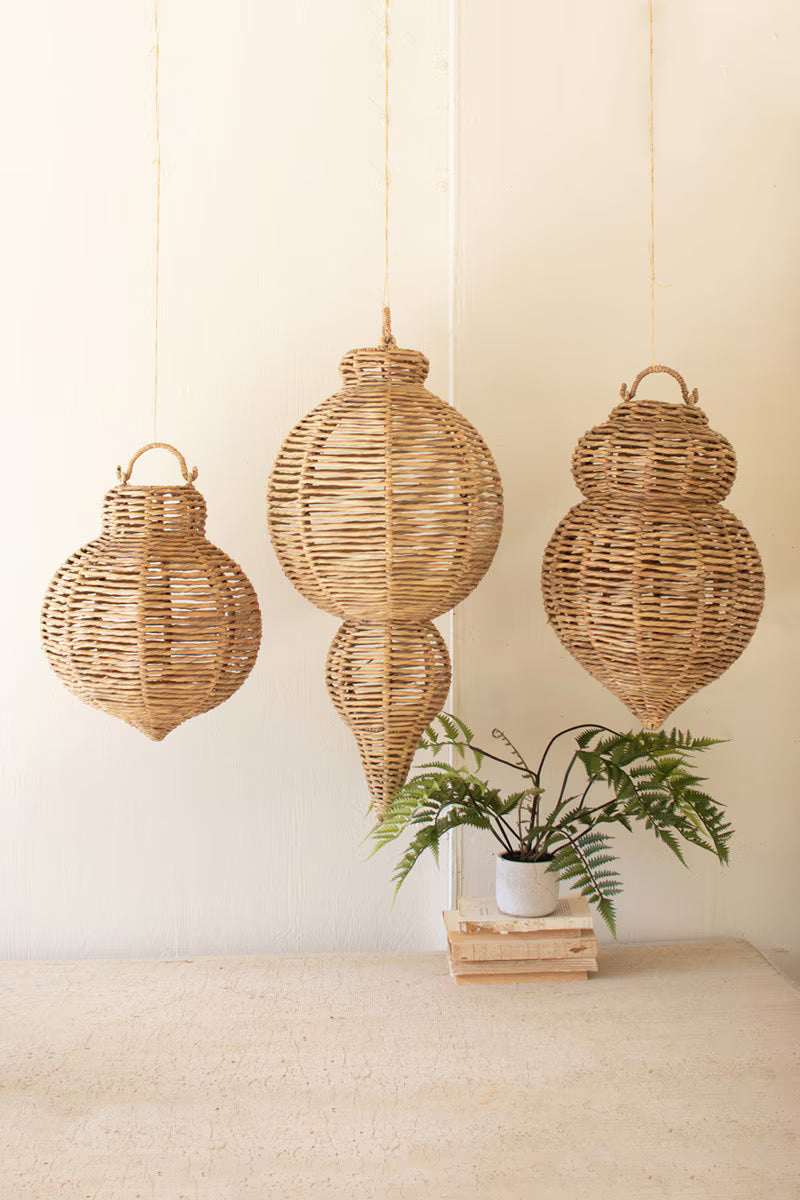 Three wicker hanging lanterns on a neutral background with a plant in the foreground.