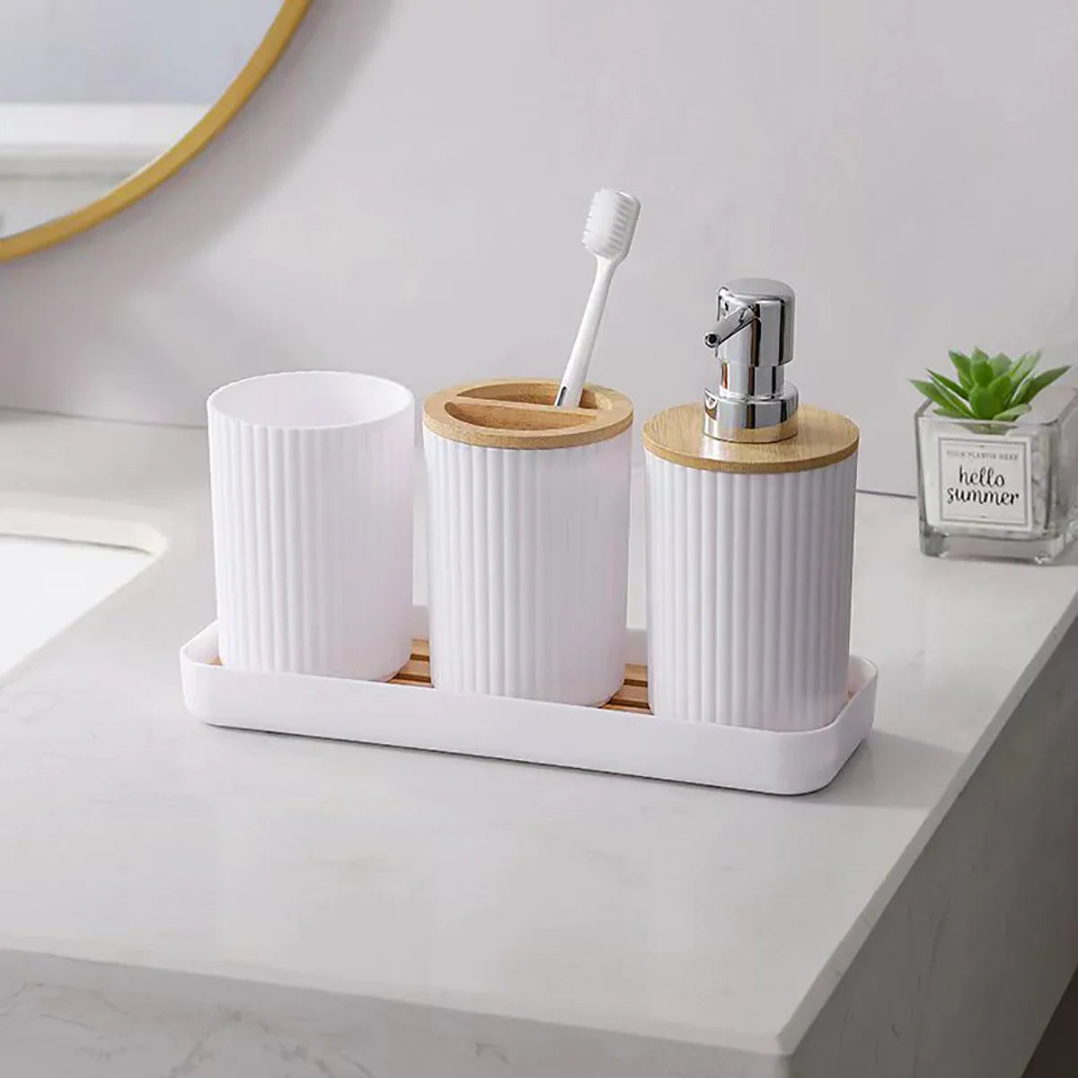 White Buddify bathroom accessories set with bamboo lids on vanity, includes soap dispenser, toothbrush holder, and cotton jar on matching tray.