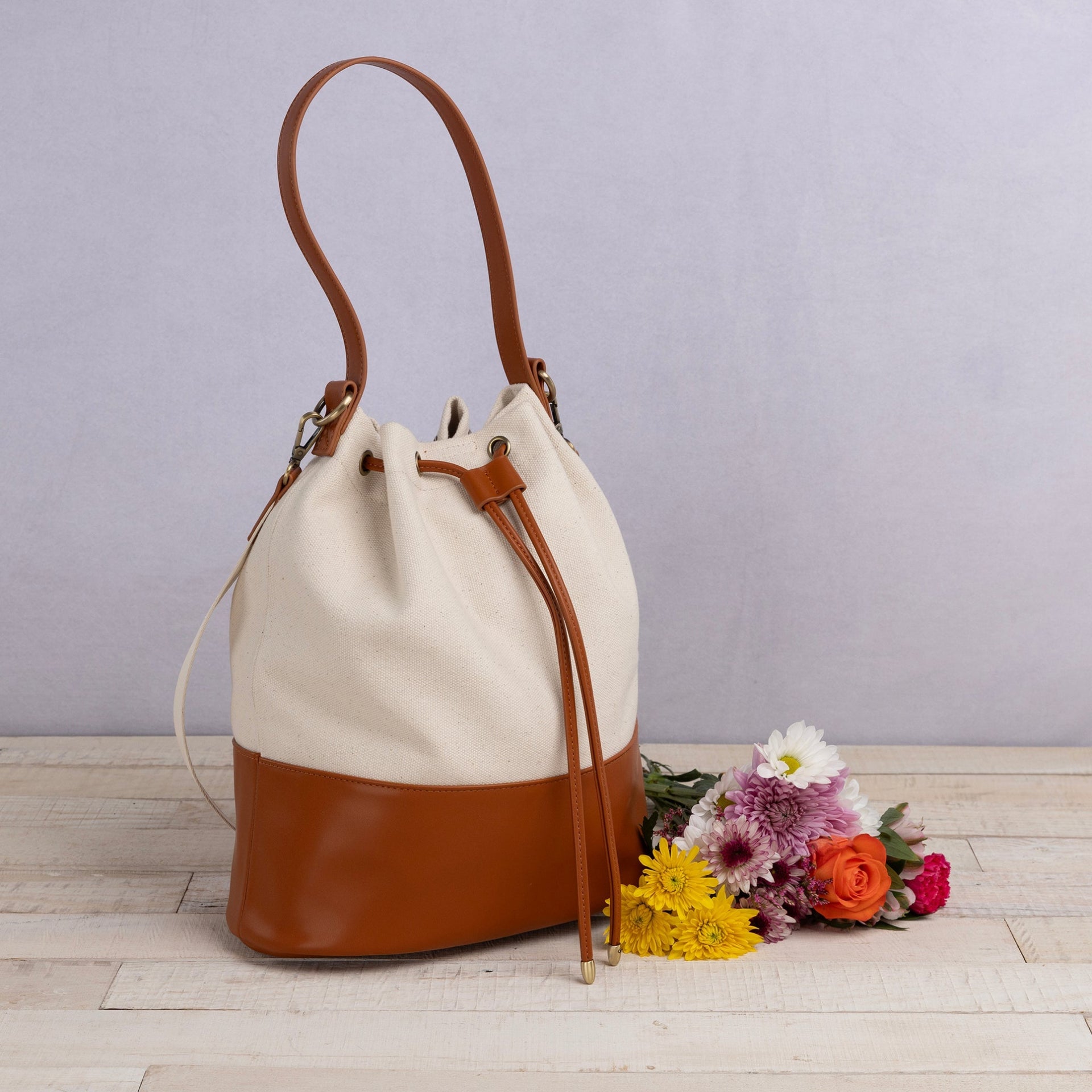 Canvas and brown leather bucket bag with flowers on a wooden surface