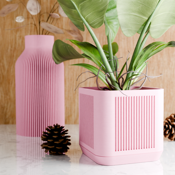 Pink textured planter with a plant and matching vase on a wooden surface