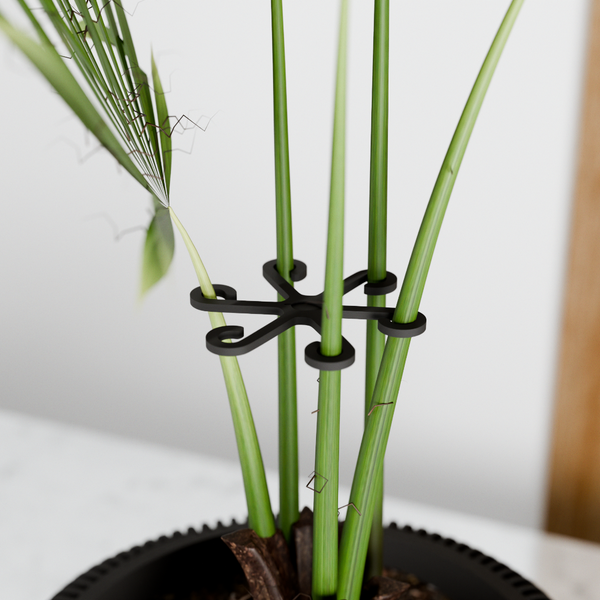 Black plant support clip holding up green plant stems against a white background