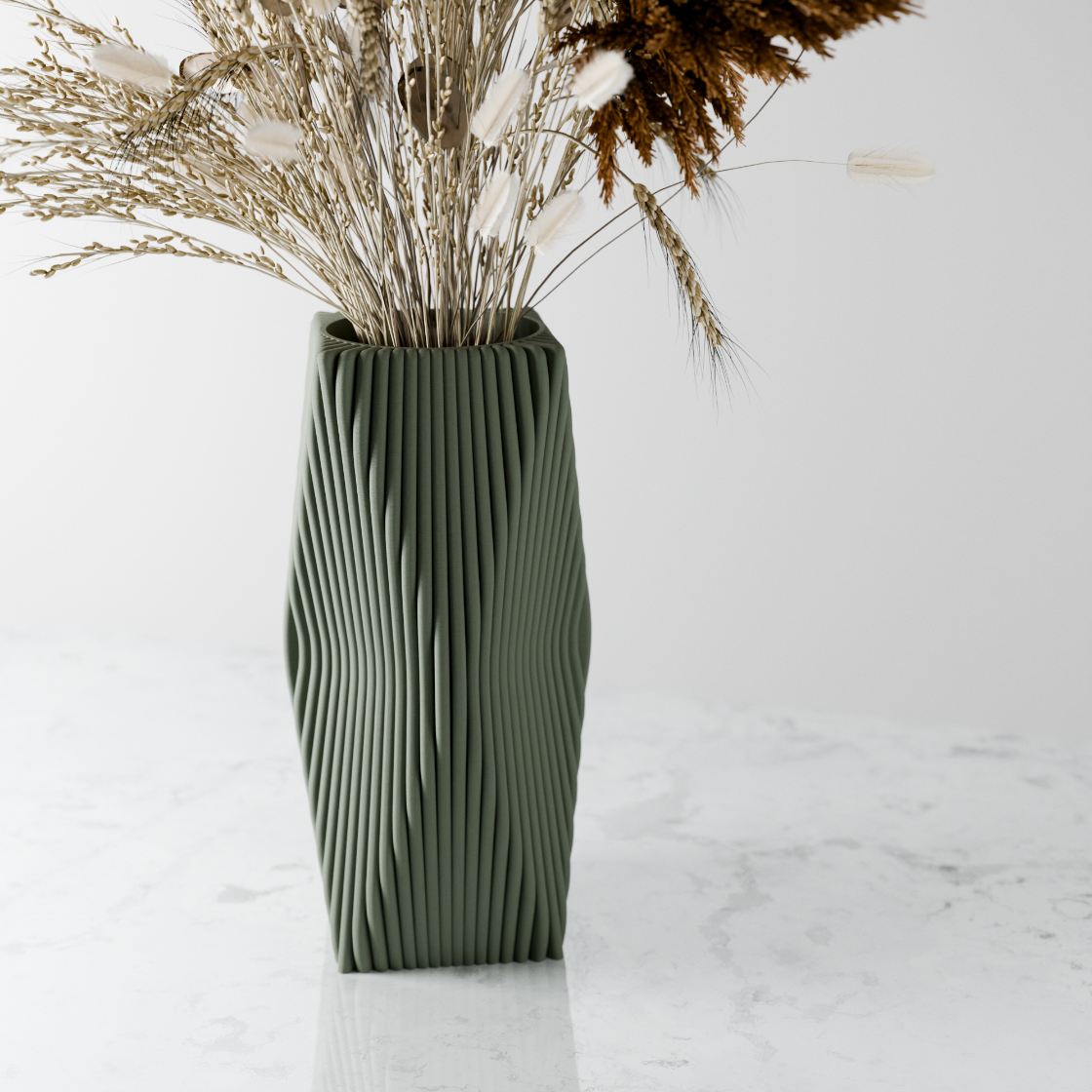 Green textured vase with dried plants on a white marble surface