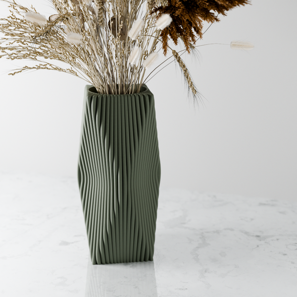 Green textured vase with dried plants on a white marble surface