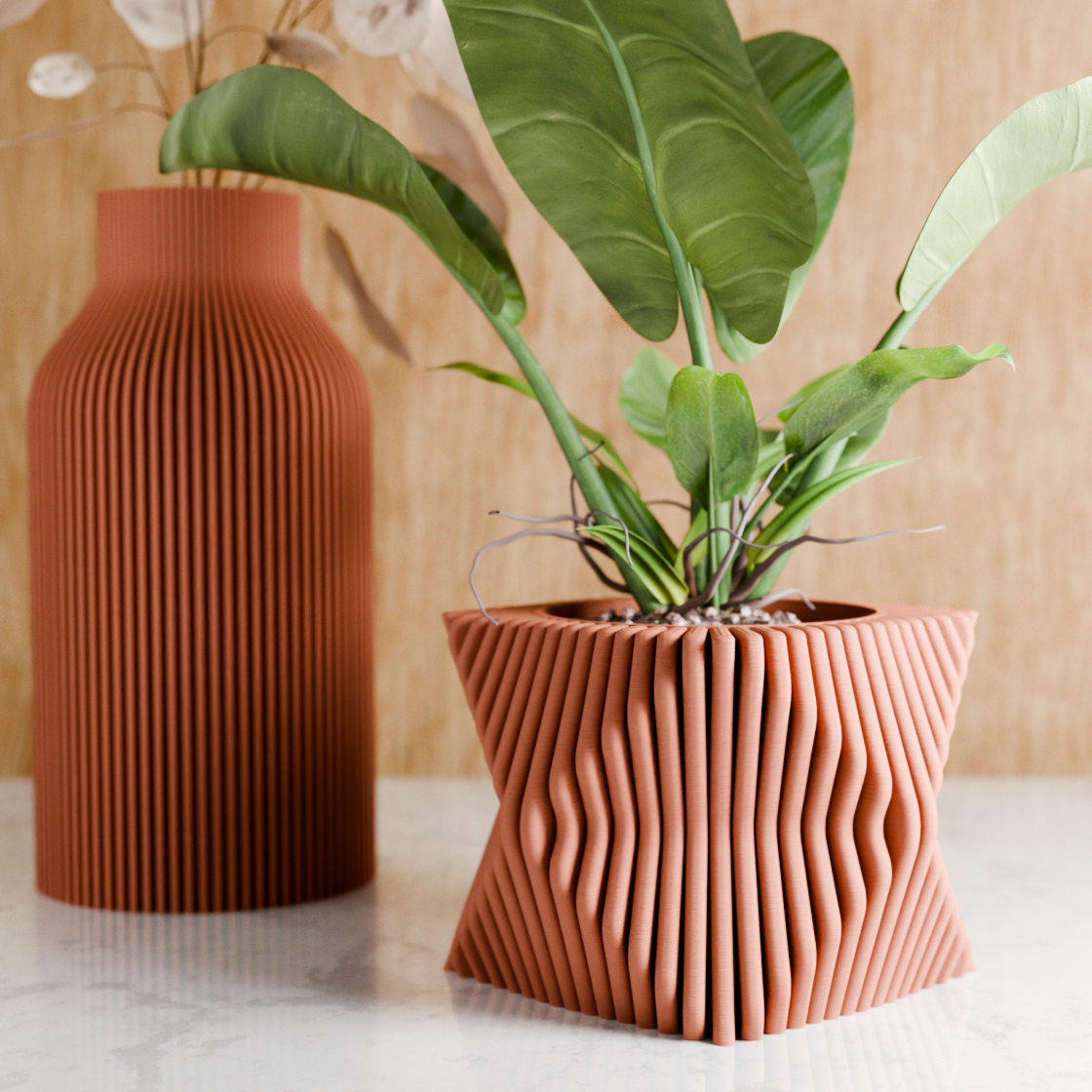 Decorative terracotta vase with wavy design next to a plant on a light surface.