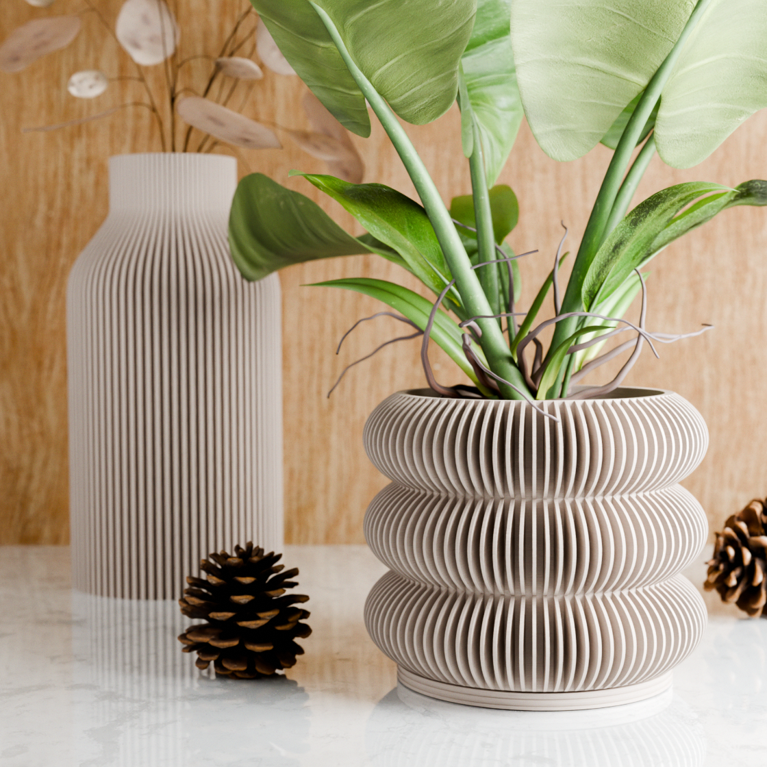 Decorative plant pot with wavy design, pinecones, and a vase on a light surface.