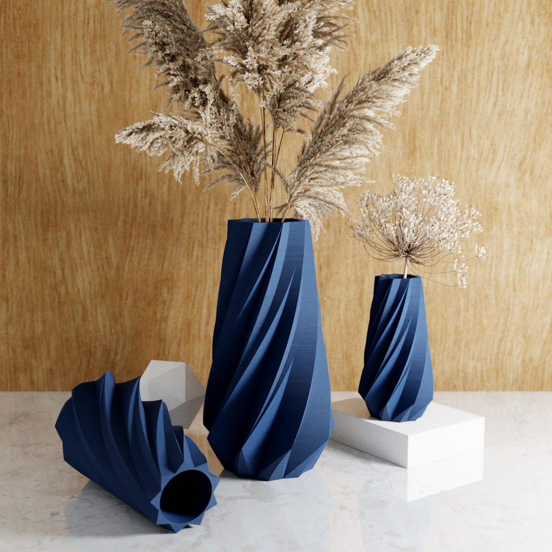 Three blue textured vases with dried plants on a marble surface against a wooden wall.