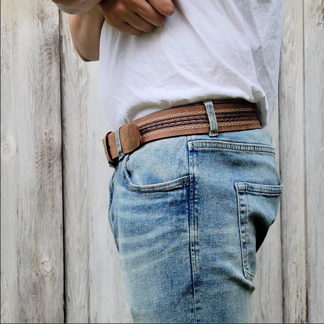 Person wearing blue jeans and a brown belt against a wooden background