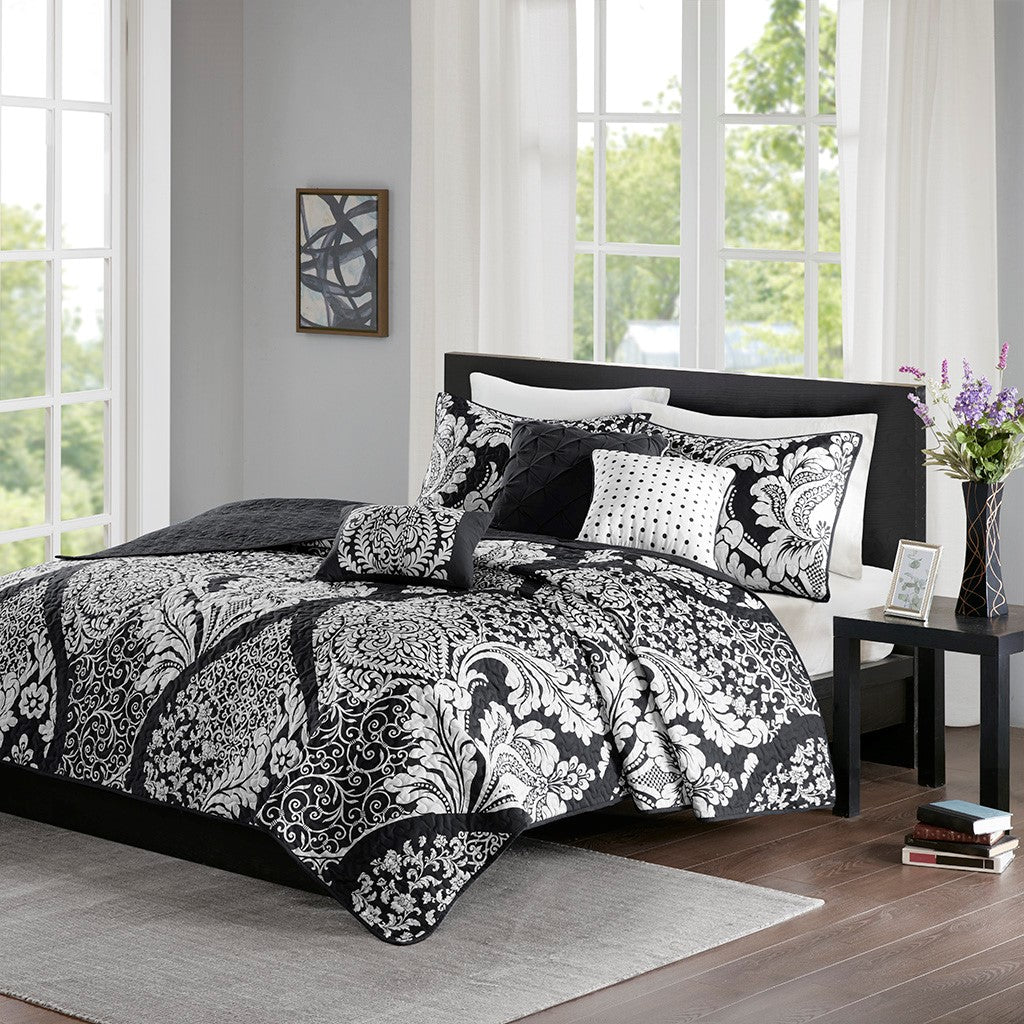 Black and white patterned bedding set on a bed in a bedroom with large windows.