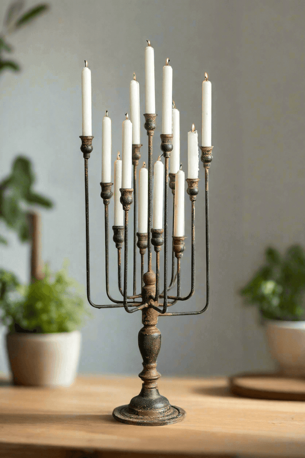 Decorative candle holder with multiple candles on a wooden surface, with plants in the background.