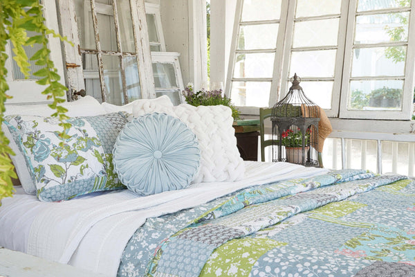 Decorative pillows on a bed with a floral quilt in a bright room.