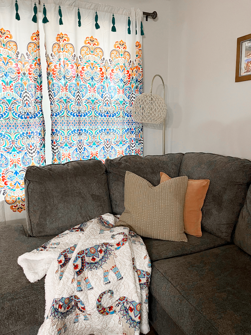 Living room with a gray sofa, colorful elephant-patterned blanket, and patterned curtains.