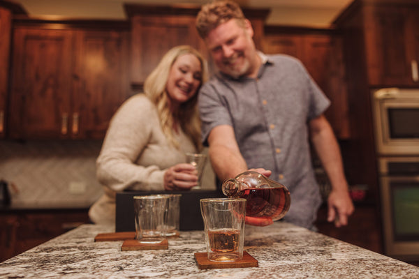 Man and woman in a kitchen pouring tea into glasses.