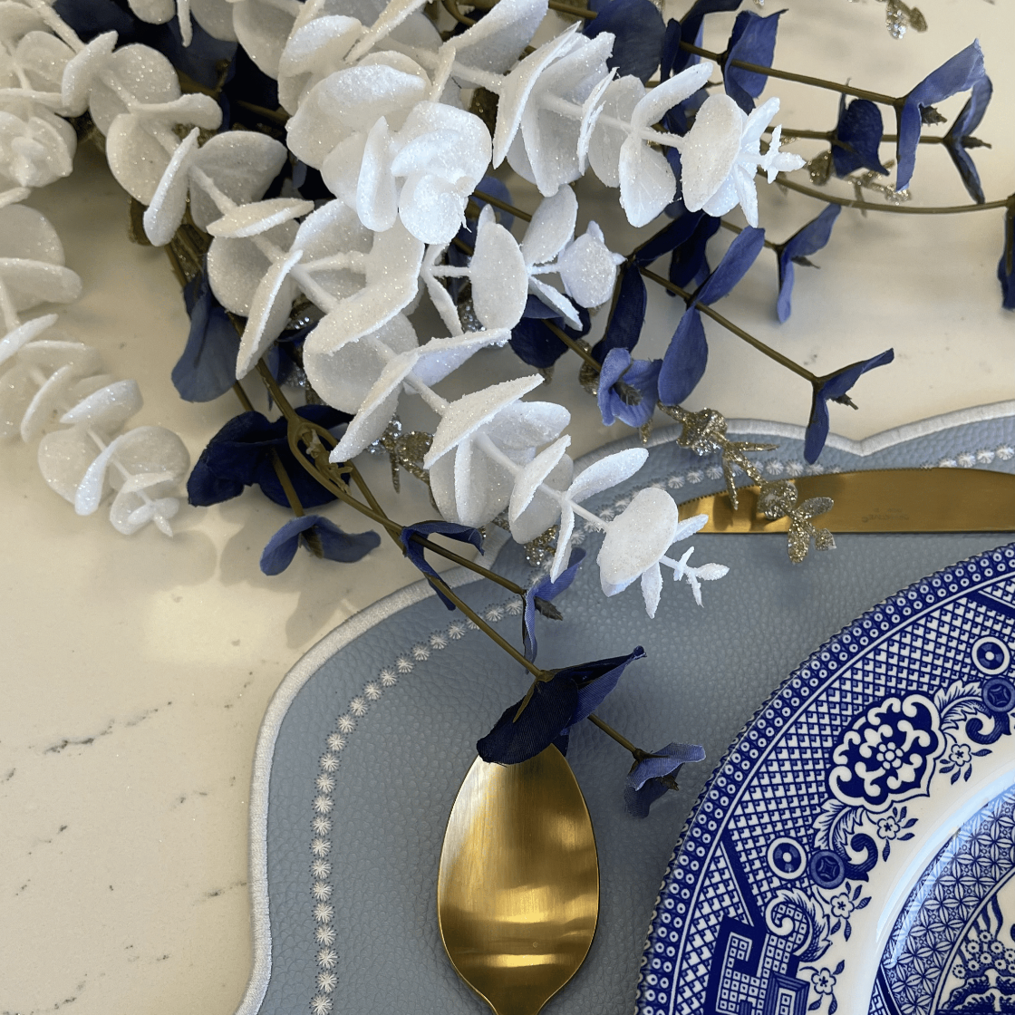 Decorative table setting with blue and white floral arrangement, gold spoon, and patterned plate.