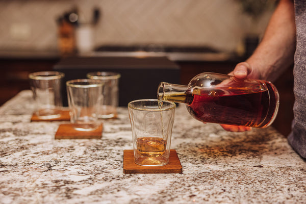 Person pouring liquid from a bottle into a glass on a kitchen counter.