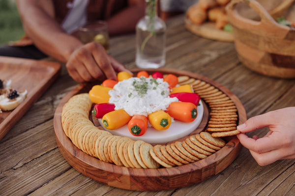 Platter of crackers and small vegetables on a wooden table with people around