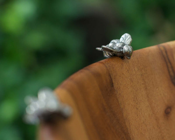 Silver fly-shaped earrings on a wooden surface with a blurred green background